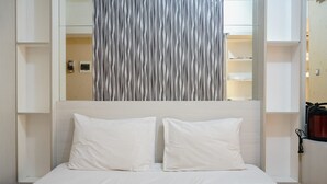 A hotel room with a bed, two pillows, a headboard, and a wall with a vertical striped pattern.