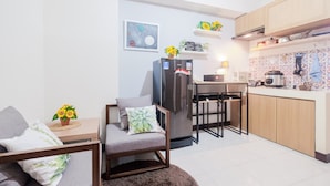A compact kitchen with a refrigerator, microwave, and wooden cabinets. There is a small dining area with a chair and a table.