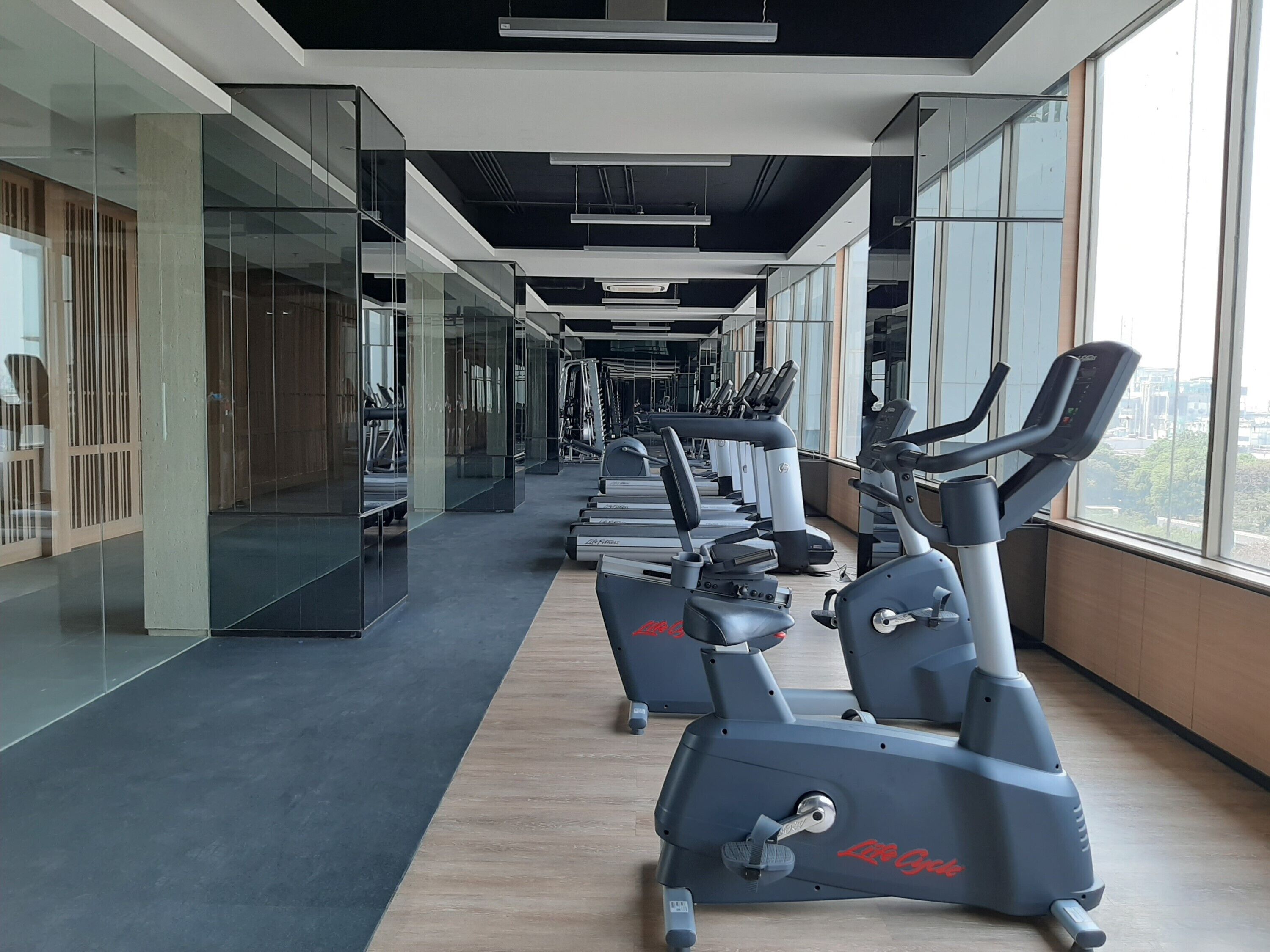 Ein Fitnessstudio mit Cardiogeräten, Glaswänden und Blick auf die Stadt.