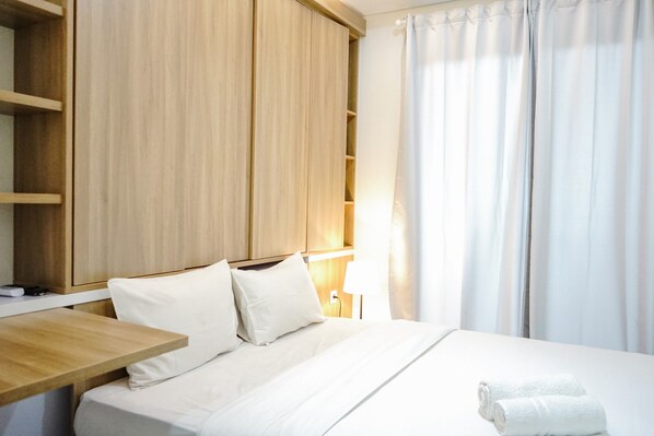 A hotel room with a bed, a wooden nightstand, a bedside table, and a wardrobe.
