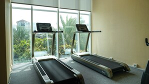 A gym with two treadmills, large windows, and a view of greenery and a building outside. - Homey and Warm 3BR Apartment at Ambassade Residences (Jakarta)