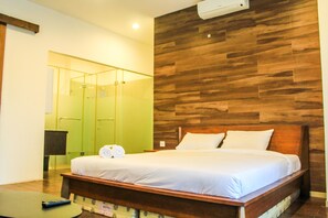 Habitación de hotel con cabecera de madera, cama con ropa blanca, mesita de noche con control remoto y espejo con marco de madera.