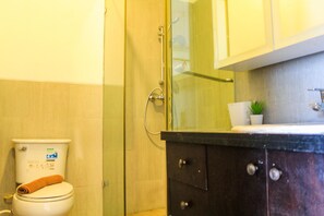 Un baño con inodoro, cabina de ducha de vidrio, lavamanos con espejo y un armario.