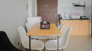 Una cocina compacta con una mesa de madera y sillas blancas, una pequeña encimera con una tetera, y una caja de servicios turísticos sobre la mesa.