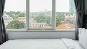 Habitación de hotel con un ventanal grande que ofrece vistas de la ciudad, con edificios y árboles.