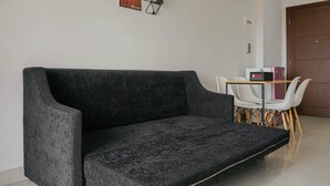 Un espacio habitable moderno con un sofá gris oscuro, una mesita con un objeto rojo y sillas blancas.