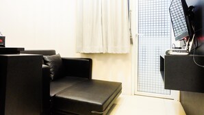 Una habitación pequeña con un sofá de cuero negro, una mesita y un televisor montado.