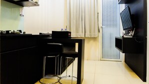 Una cocina compacta con estufa a gas, taburetes negros, una mesa pequeña y un televisor montado en la pared.