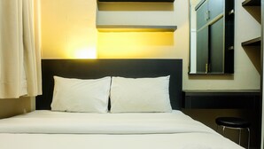 Una cama bien hecha con sábanas y almohadas blancas, un taburete a un lado y un mueble de pared con espejo.