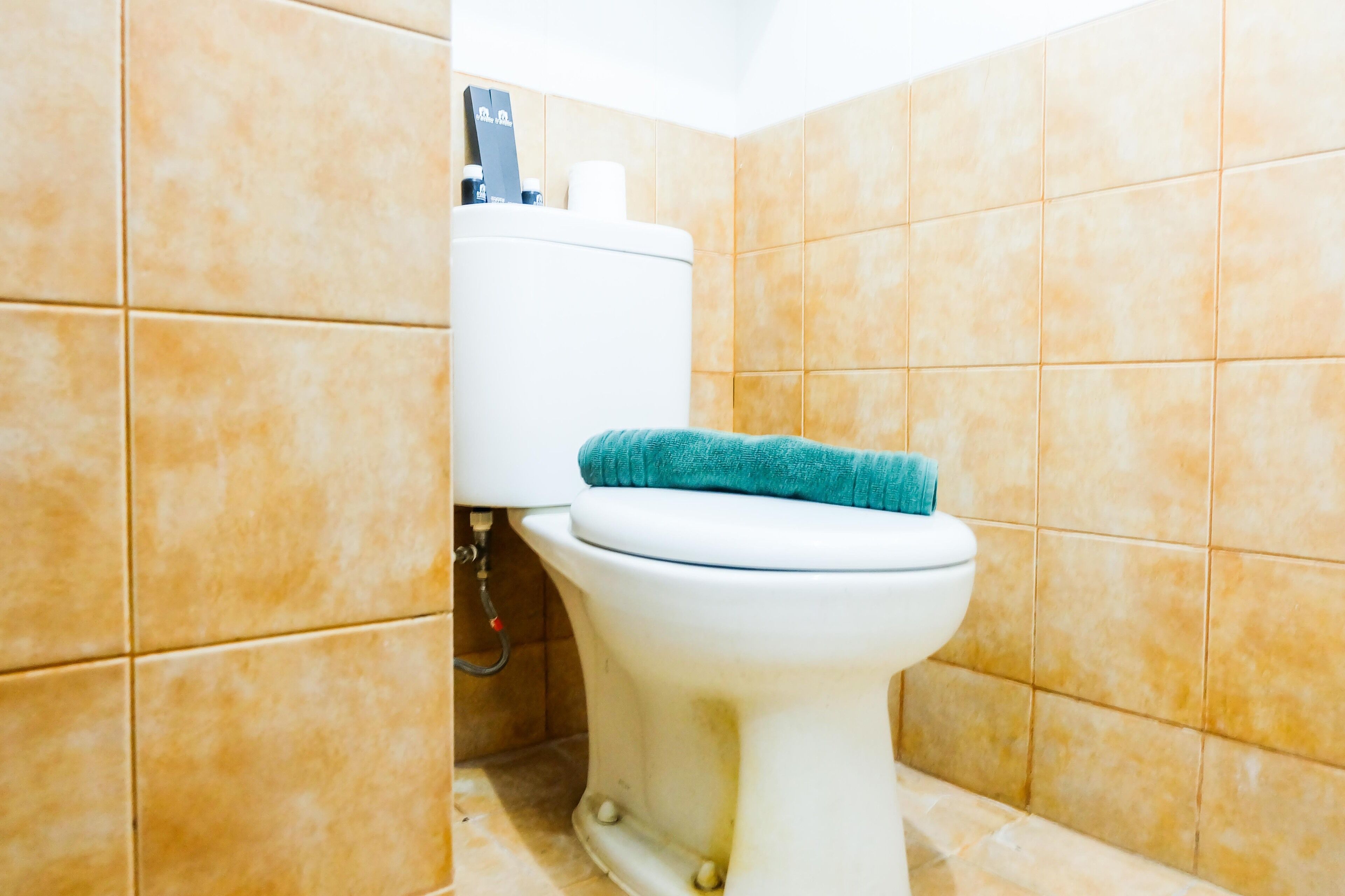 Une salle de bain avec des toilettes blanches, des murs recouverts de carreaux beiges et un tapis de bain bleu.