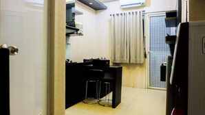 Cocina compacta con encimera negra, dos taburetes y un equipo de aire acondicionado en la pared.