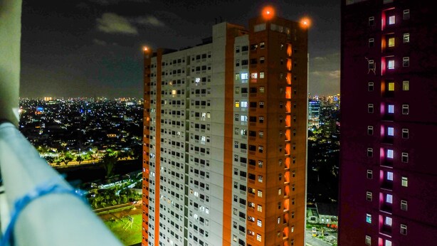 Un edificio alto con varios pisos, ventanas amplias y vistas de un paisaje urbano nocturno.