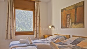 Une chambre avec deux lits, une fenêtre avec des rideaux, un tableau au mur et une lampe de chevet.