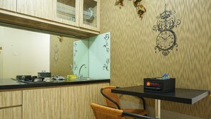 A kitchen with a wooden cabinet, a black countertop, a wicker chair, and a wall clock.