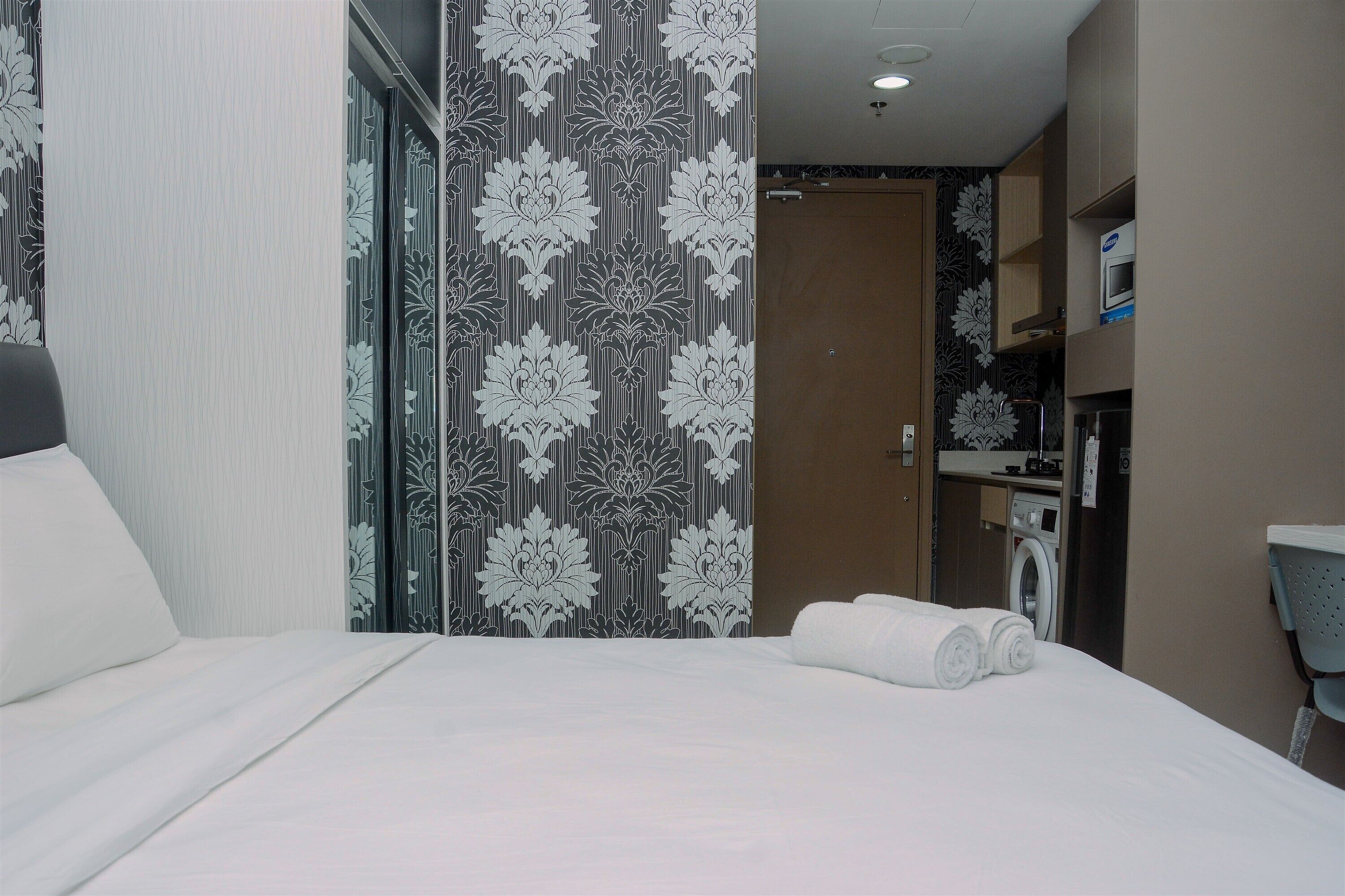 A hotel room with a bed, a washing machine, and a microwave in the kitchenette.