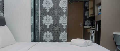 A hotel room with a bed, a washing machine, and a microwave in the kitchenette.