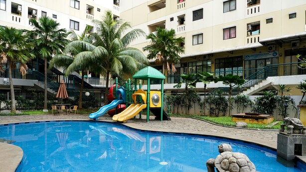 A swimming pool with a slide, palm trees, and a play structure. - Comfortable and Homey Studio Apartment at Kebagusan City (Jakarta)