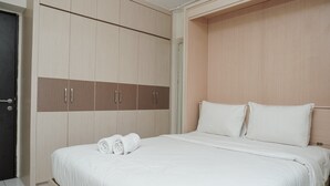 A neatly made bed with white linens, a wooden wardrobe with two drawers, and a door. - Comfortable and Homey Studio Apartment at Kebagusan City (Jakarta)