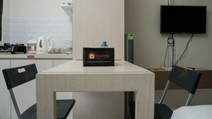 A hotel room with a kitchenette, a flat-screen TV mounted on the wall, and a table with chairs. - Comfortable and Homey Studio Apartment at Kebagusan City (Jakarta)