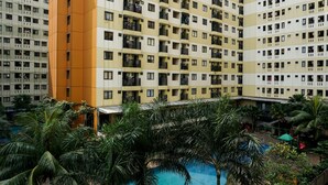 A high-rise building with multiple balconies, a swimming pool, and surrounding greenery. - Comfortable and Homey Studio Apartment at Kebagusan City (Jakarta)