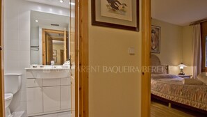 Une chambre d’hôtel avec un plancher en bois, un lit recouvert d’une couvre-lit beige, une table de chevet avec une lampe et une salle de bain équipée de toilettes et d’un lavabo.
