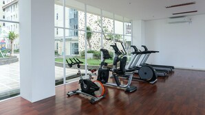 A gym with exercise equipment, large windows, and a view of buildings and greenery outside. - Fully Furnished 1BR Apartment at Vittoria Residence (Jakarta)