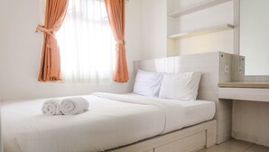 A neatly made bed with white linens and two rolled towels, a bedside table, a mirror, and a window with curtains. - Warm and Cozy 2BR Green Pramuka Apartment near Mall (Jakarta)