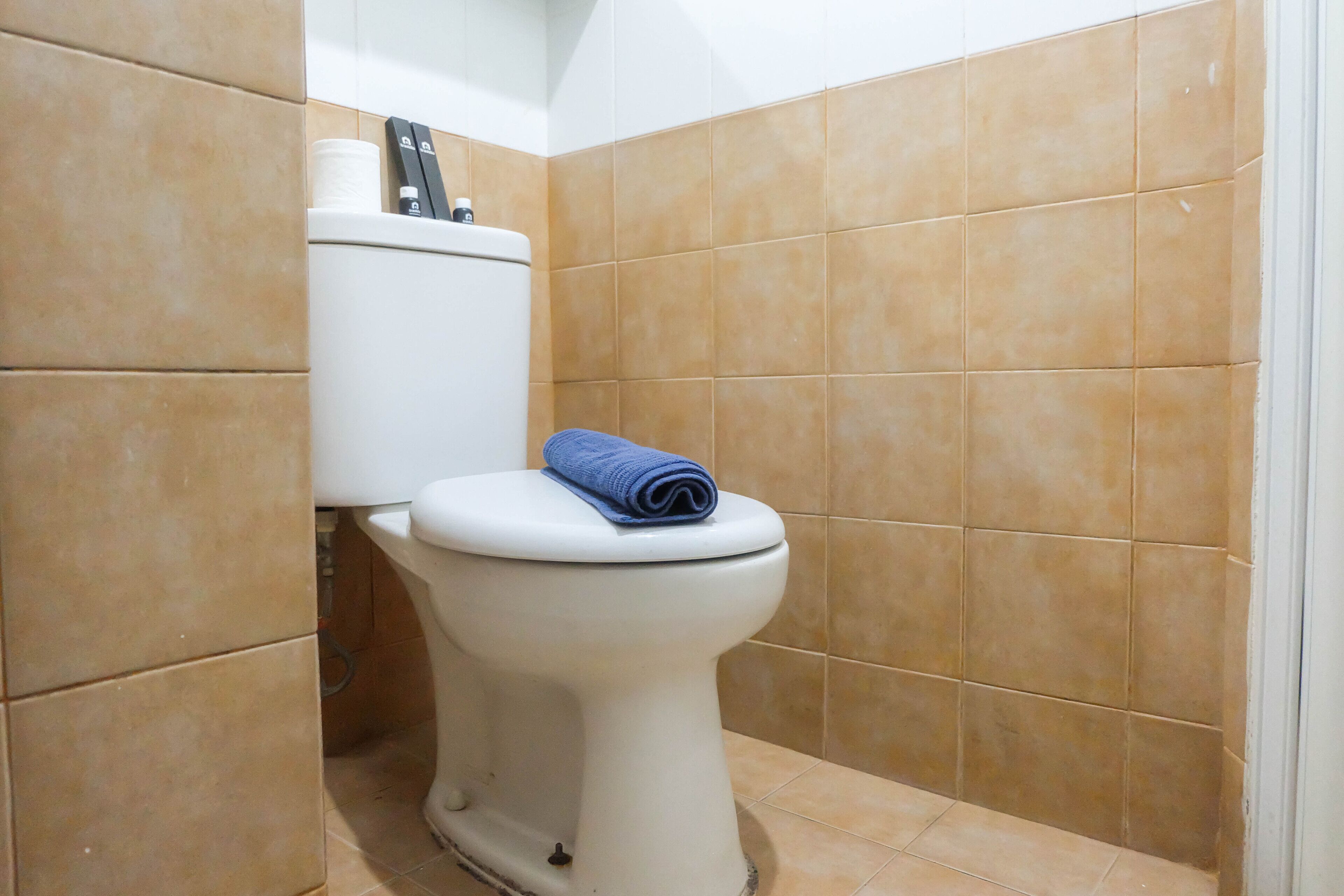 Een badkamer met een wit toilet, beige tegels en een blauwe handdoek op de zitting.