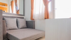 A modern living room with a grey sofa, a wooden headboard, and a large mirror. - Warm and Cozy 2BR Green Pramuka Apartment near Mall (Jakarta)