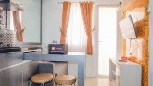 A modern kitchen with a built-in stove, a sink, and a countertop with a coffee machine. There are two stools and a small table with a tray of condiments. - Warm and Cozy 2BR Green Pramuka Apartment near Mall (Jakarta)