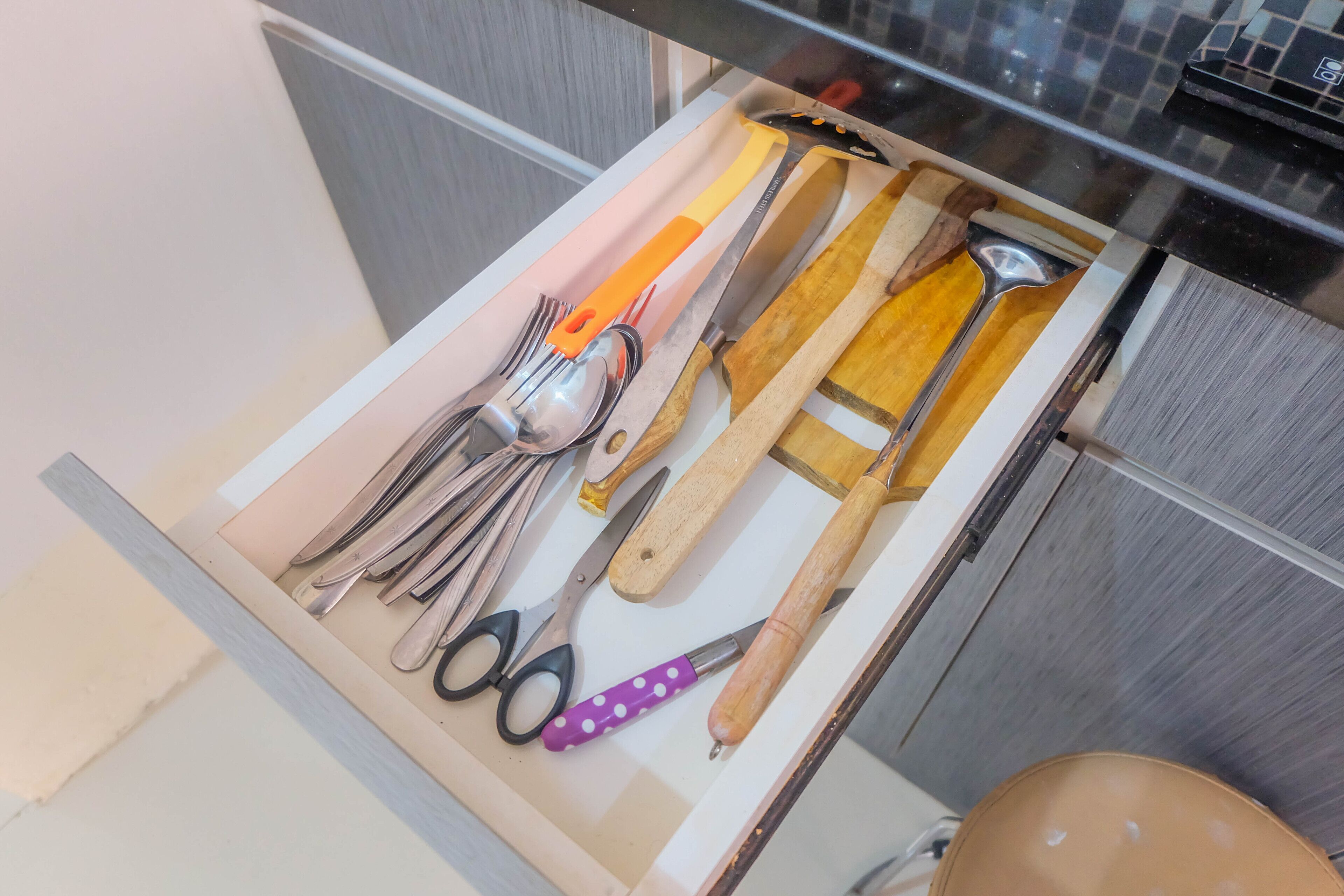 A drawer with various kitchen utensils including spoons, forks, knives, scissors, and a hammer.