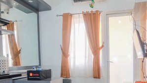 A modern hotel room with a kitchenette, a seating area with stools, a large mirror, and a door leading to the outside. - Warm and Cozy 2BR Green Pramuka Apartment near Mall (Jakarta)
