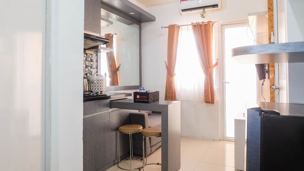 A modern kitchen with a built-in stove, a small bar area with stools, and a window with curtains. - Warm and Cozy 2BR Green Pramuka Apartment near Mall (Jakarta)