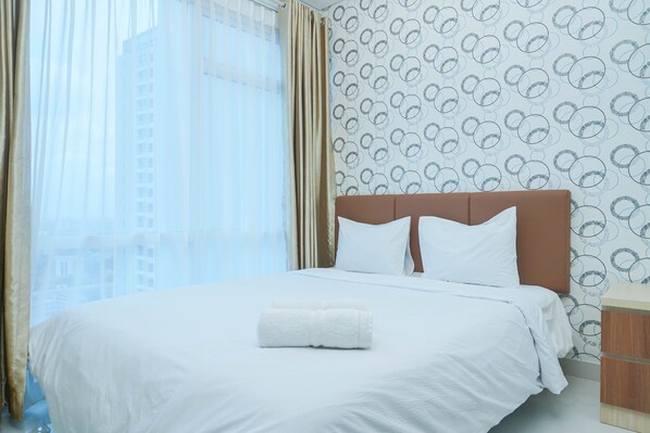 A hotel room with a large bed, white bedding, a brown headboard, and a window with curtains.