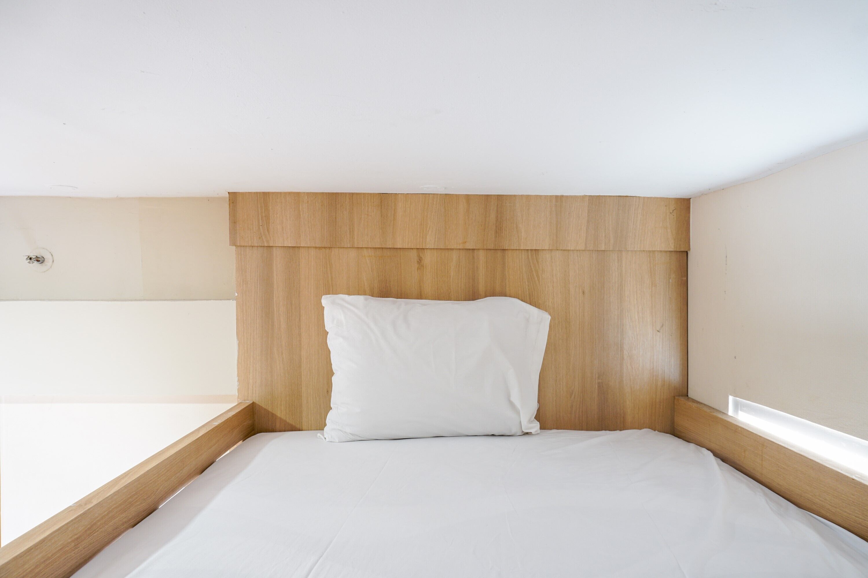 Una cama individual con cabecera de madera y almohada blanca en una habitación minimalista.