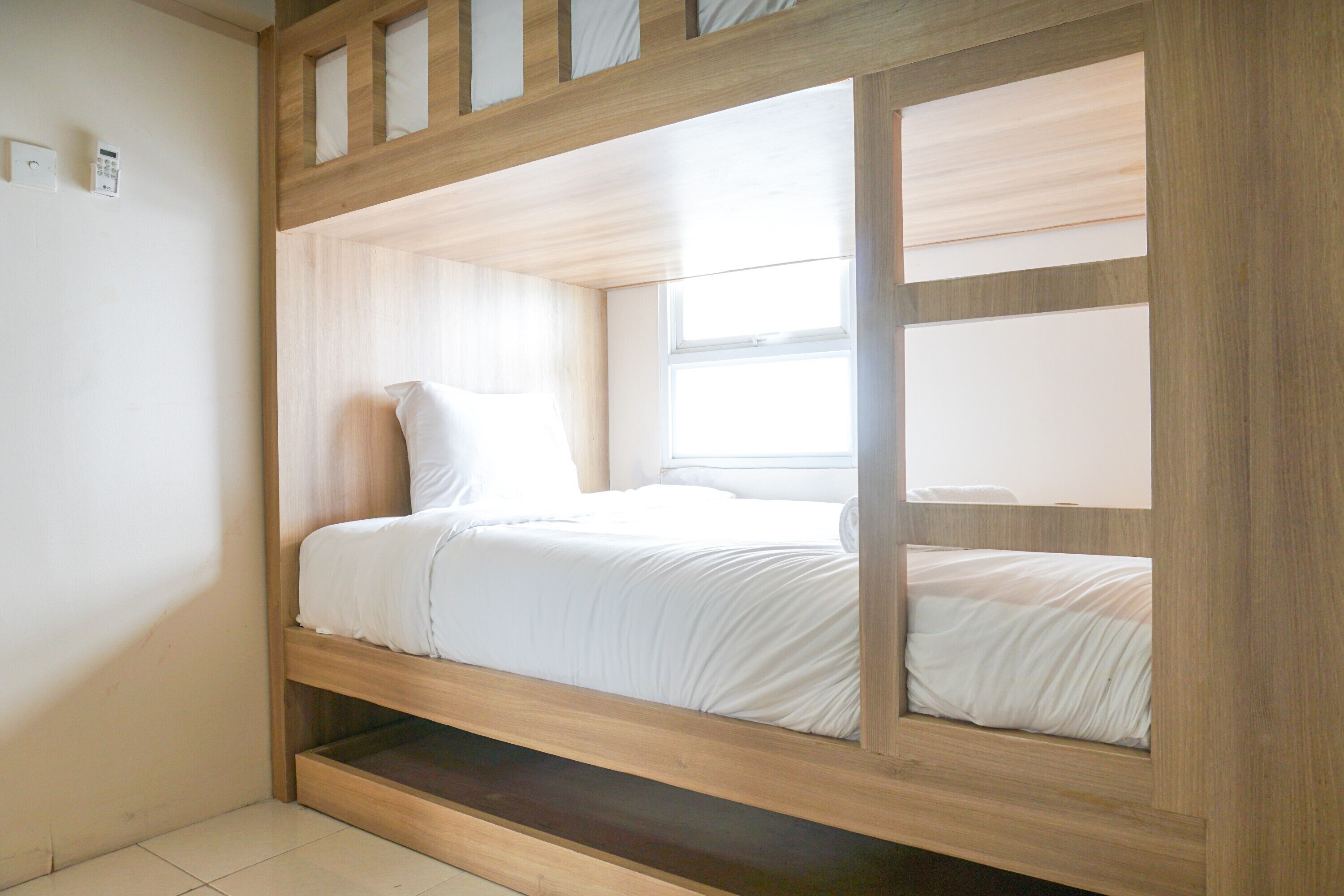 Una cama litera con estructura de madera, ropa de cama blanca y una ventana con persianas.