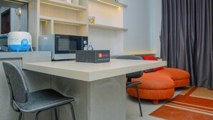 Ein modernes Hotelzimmer mit einer Küchenzeile, einer Mikrowelle, einer Reisetasche, einem grauen Sessel und einem orangefarbenen Sofa.