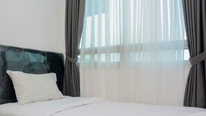 Ein ordentlich bezogenes Bett mit weißen Leinen, einem dunklen Kopfteil und transparenten Vorhängen, die natürliches Licht hereinlassen.