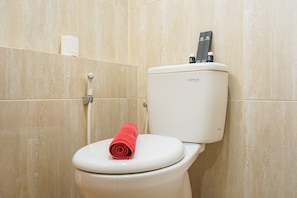 A toilet with a white seat and lid, a red towel on the seat, and a toilet paper roll on the wall.