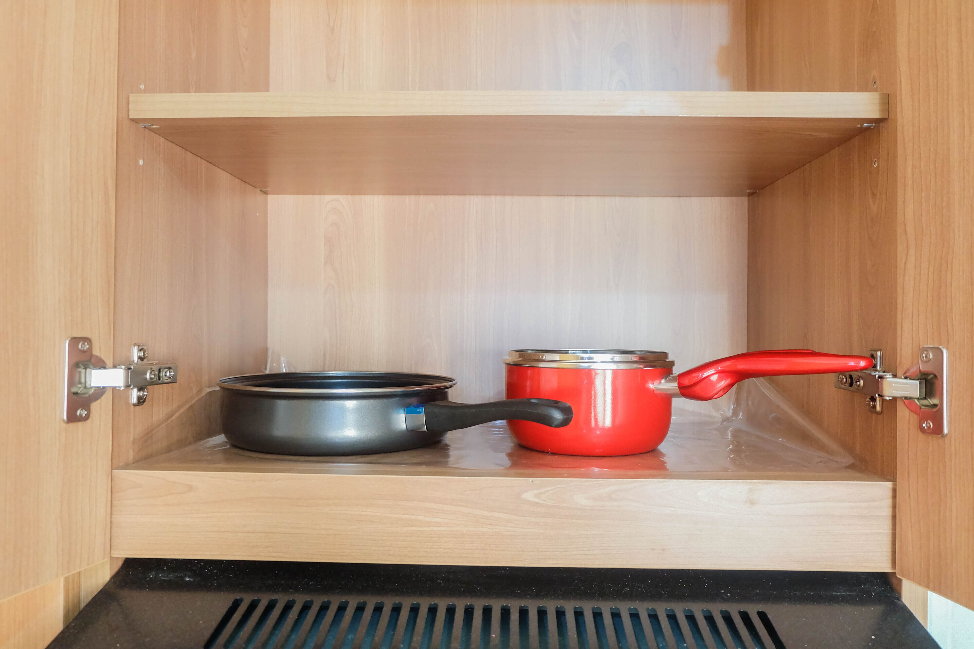 A kitchen cabinet with two pots, one red and one black, and a wooden shelf above.