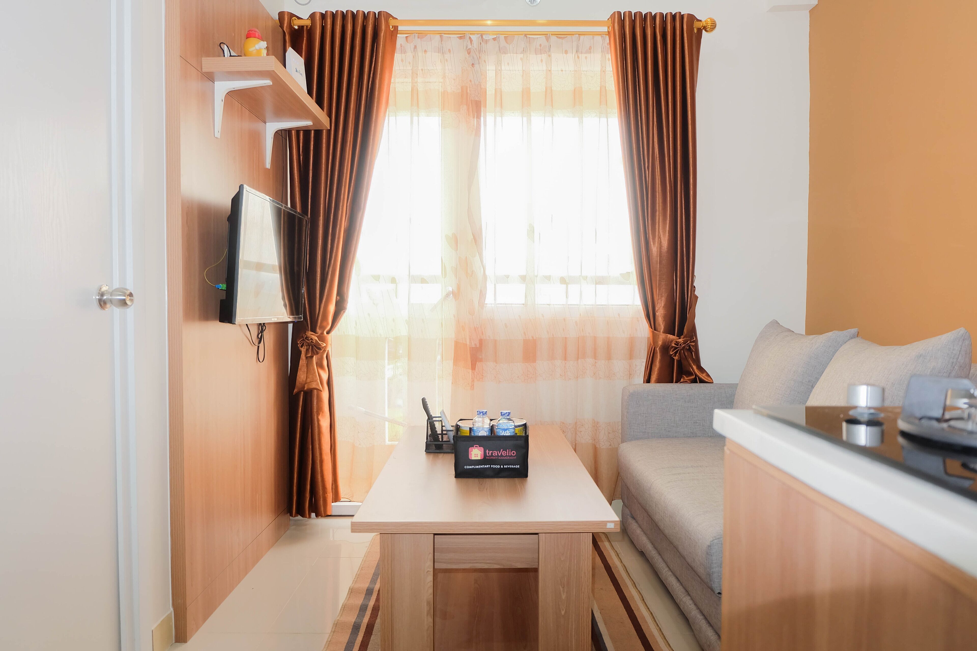 A compact room with a sofa, a small table, a TV, and a window with curtains.
