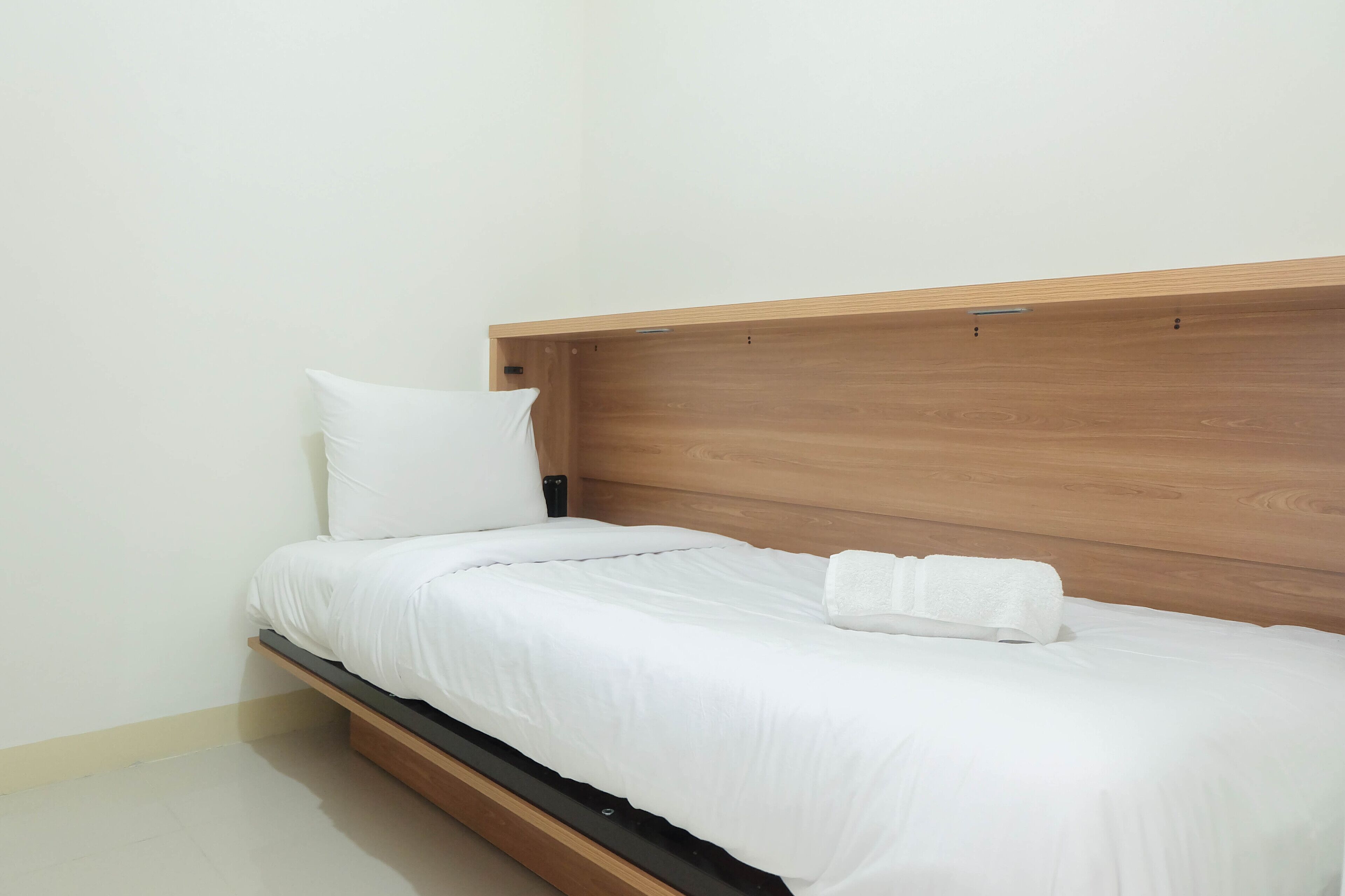 A single bed with a wooden headboard, white bedding, and a white pillow.