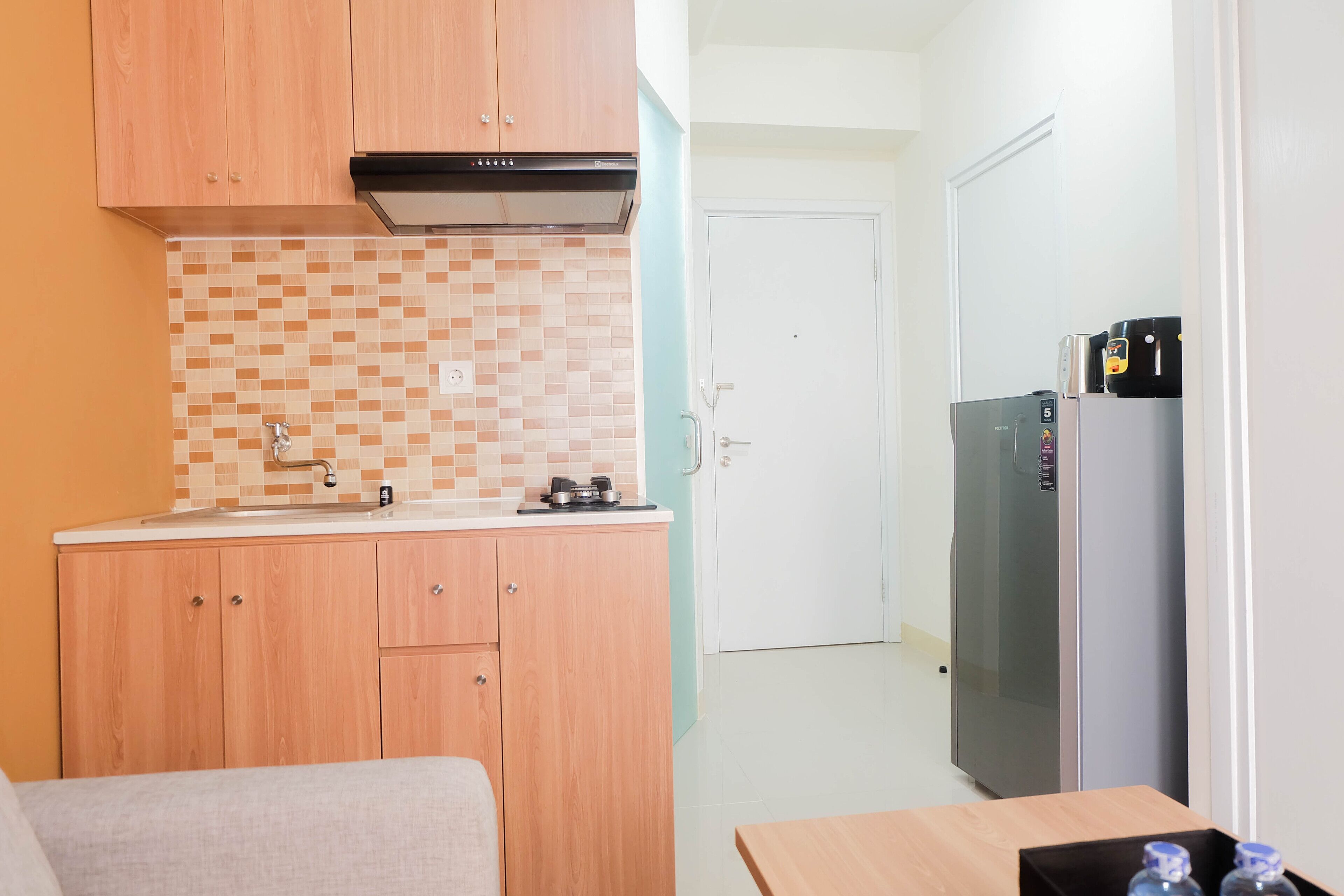 A compact kitchen with wooden cabinets, a tiled backsplash, a stainless steel sink, and a refrigerator.