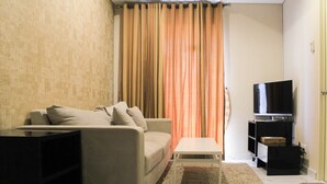 Uma sala de estar com sofá, mesa de centro, televisão e cortina.