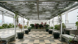 Uma área externa coberta com piso xadrez, plantas em vasos e bancos.