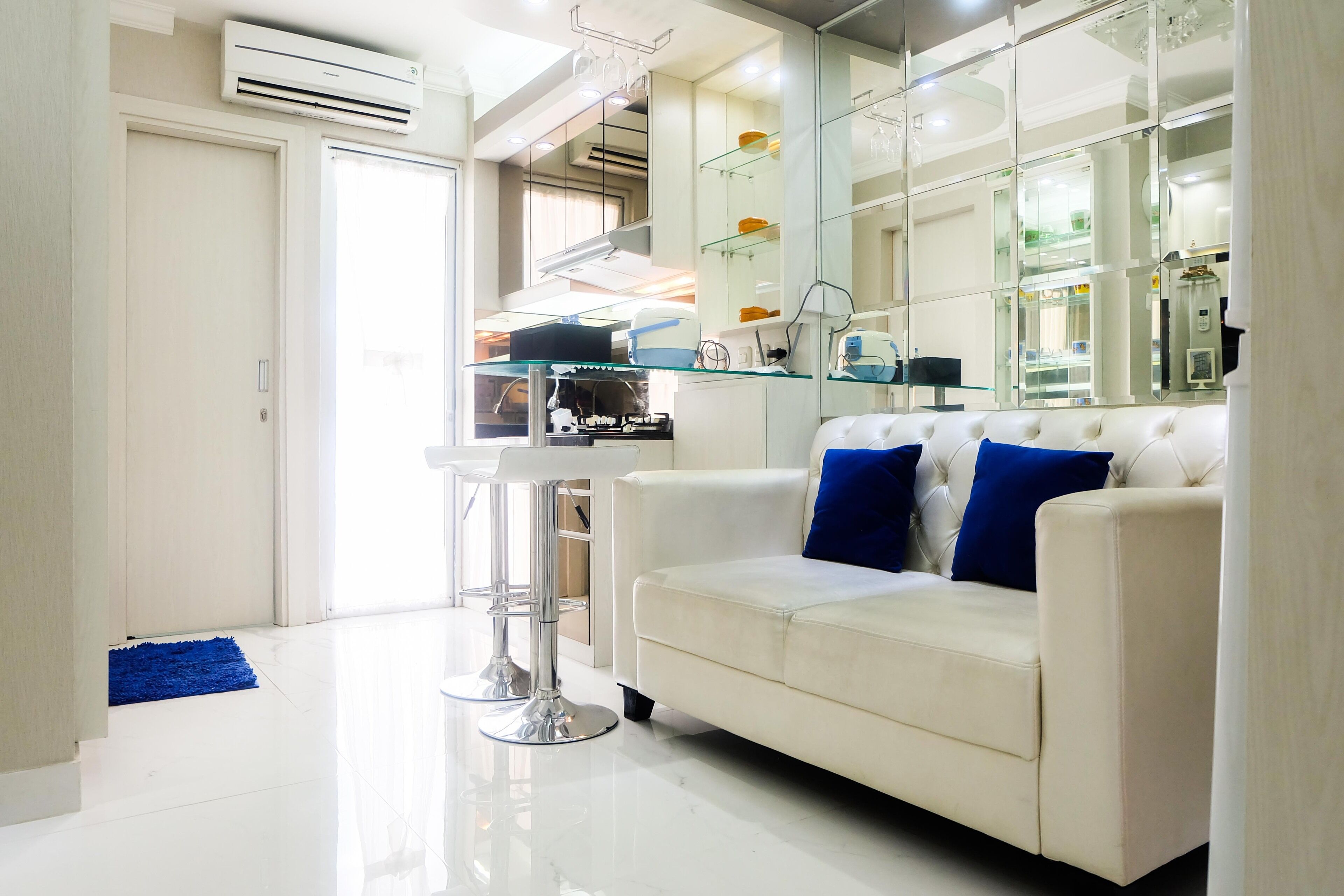 Una sala de estar moderna con un sofá blanco, un aparador de vidrio y piso blanco.