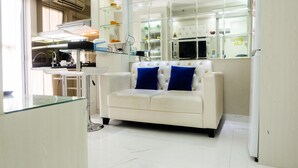 A modern kitchen with a white countertop, a glass dining table, and a white sofa with blue cushions. - Posh 2BR Apartment at Bassura City near Shopping Mall (Jakarta)