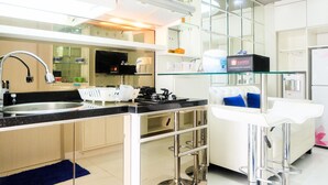 A modern kitchen with a gas stove, stainless steel sink, and glass-fronted cabinets. There is a bar area with stools and a minibar. - Posh 2BR Apartment at Bassura City near Shopping Mall (Jakarta)