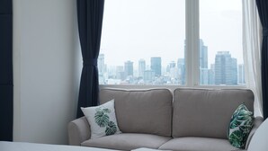 A modern living room with a sofa and a city view through large windows. - Cozy and Tranquil Studio Menteng Park Apartment (Jakarta)