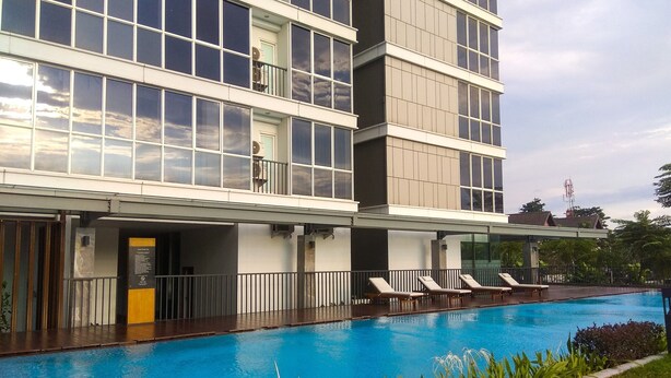 A modern hotel with a swimming pool, multiple balconies, and a well-maintained garden area. - Big Size with City View @ 3BR Lexington Apartment (Jakarta)